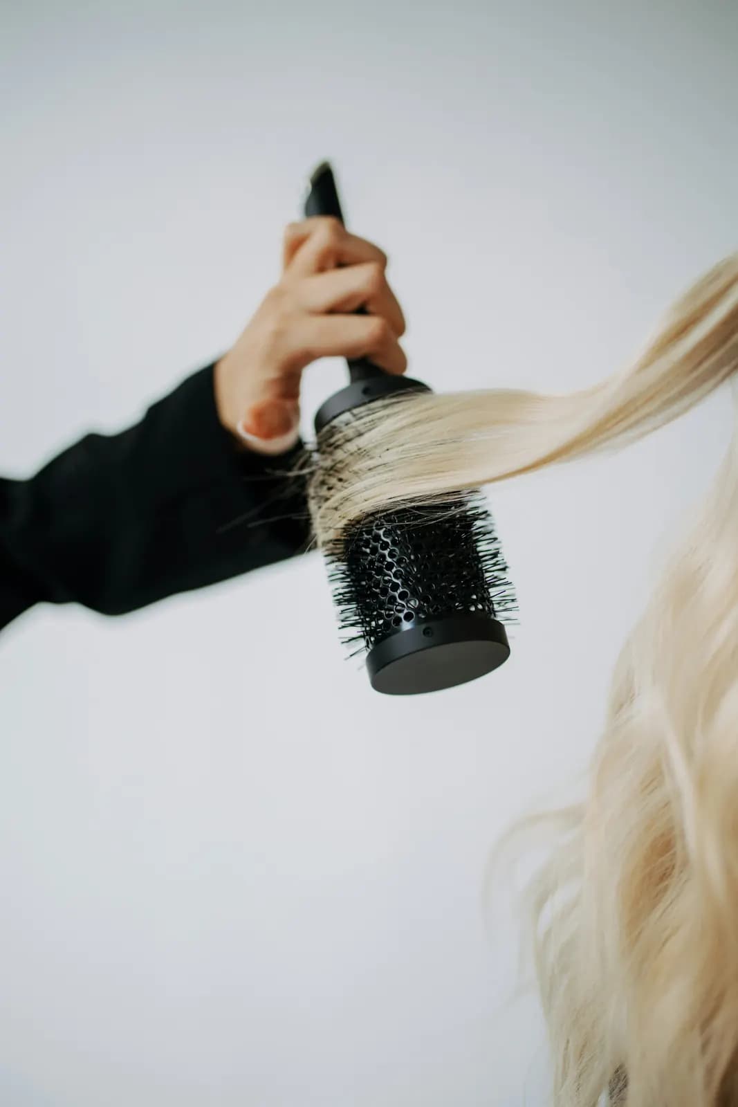 A hand lifting a lock of long blonde hair with a round brush