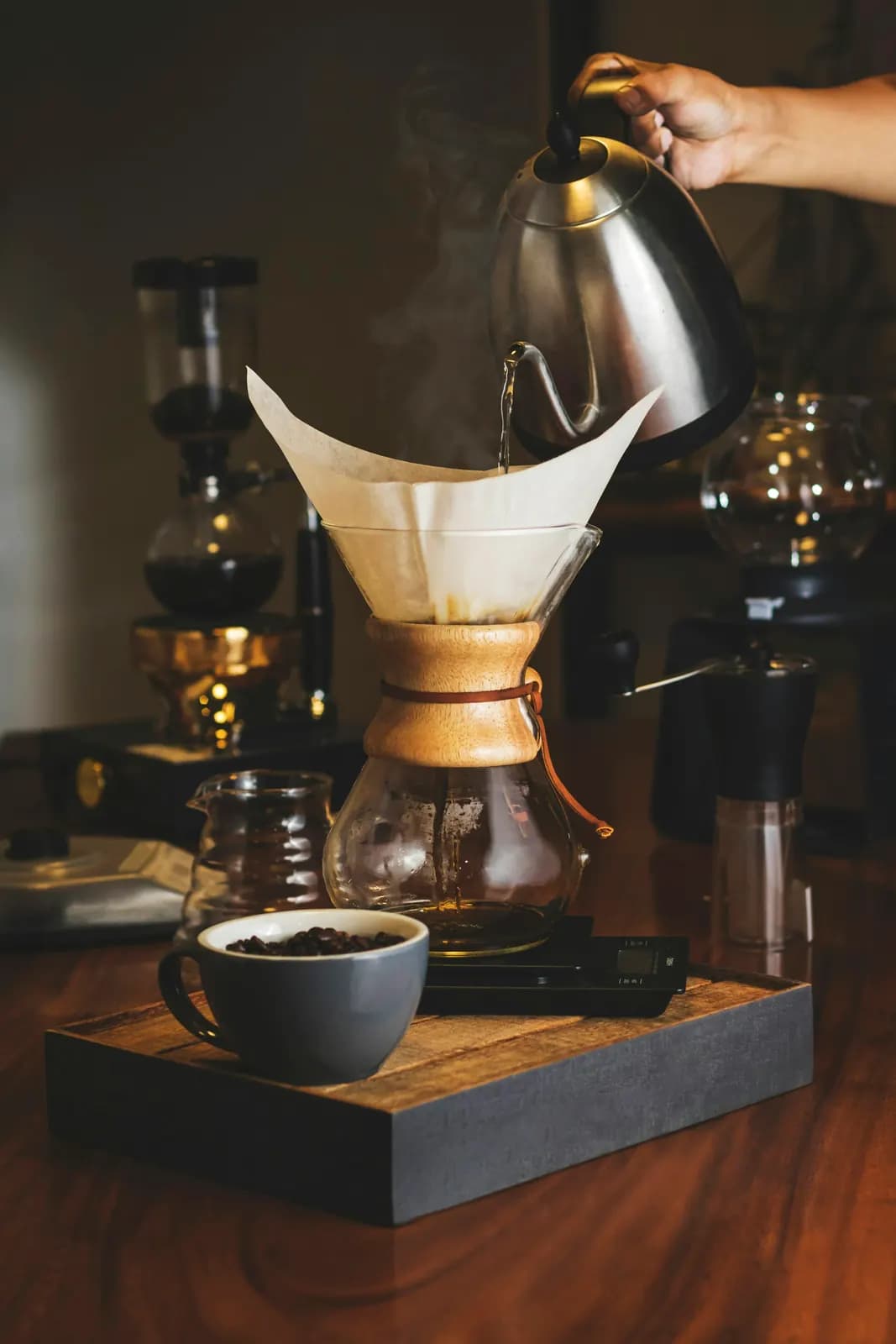 Water pouring from a gooseneck kettle into a Chemex on a wooden tray