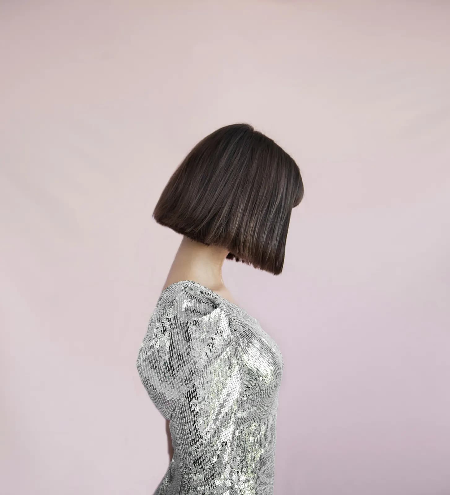 A sleek, dark blunt bob from the side and behind, against a blush-pink wall