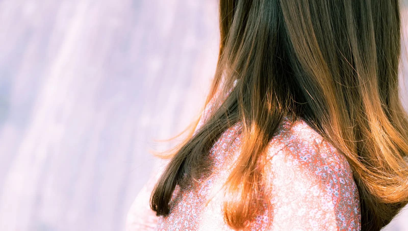 Long dark hair fading to copper at the ends, over a pink floral blouse