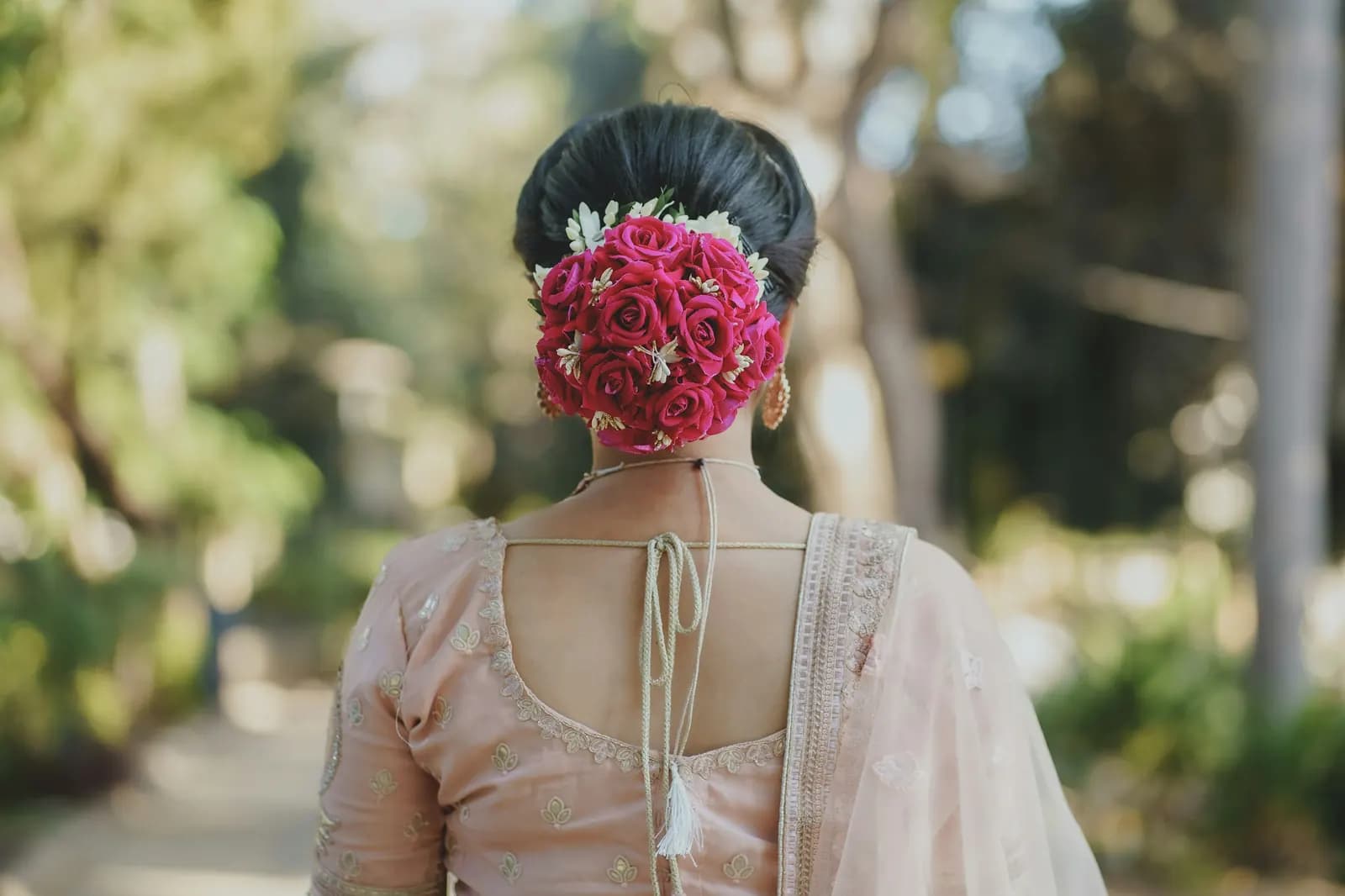 Seen from behind, a sleek black low bun covered in pink roses and small white flowers