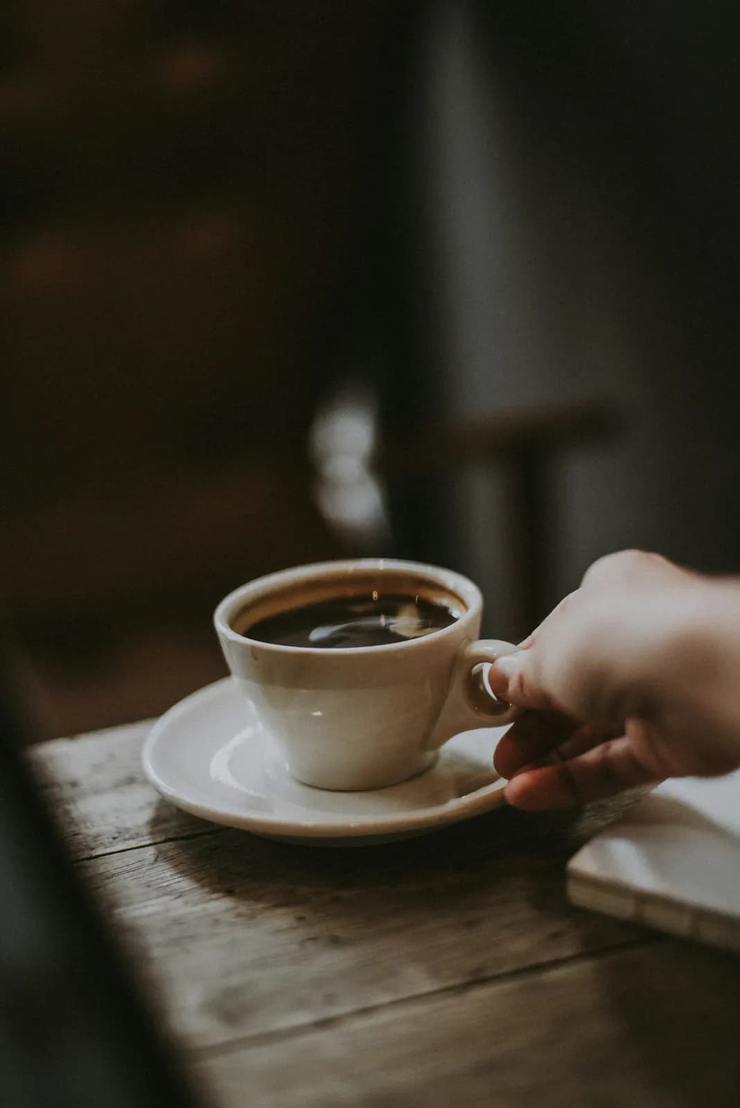 A hand setting a cup of black coffee on a wooden counter