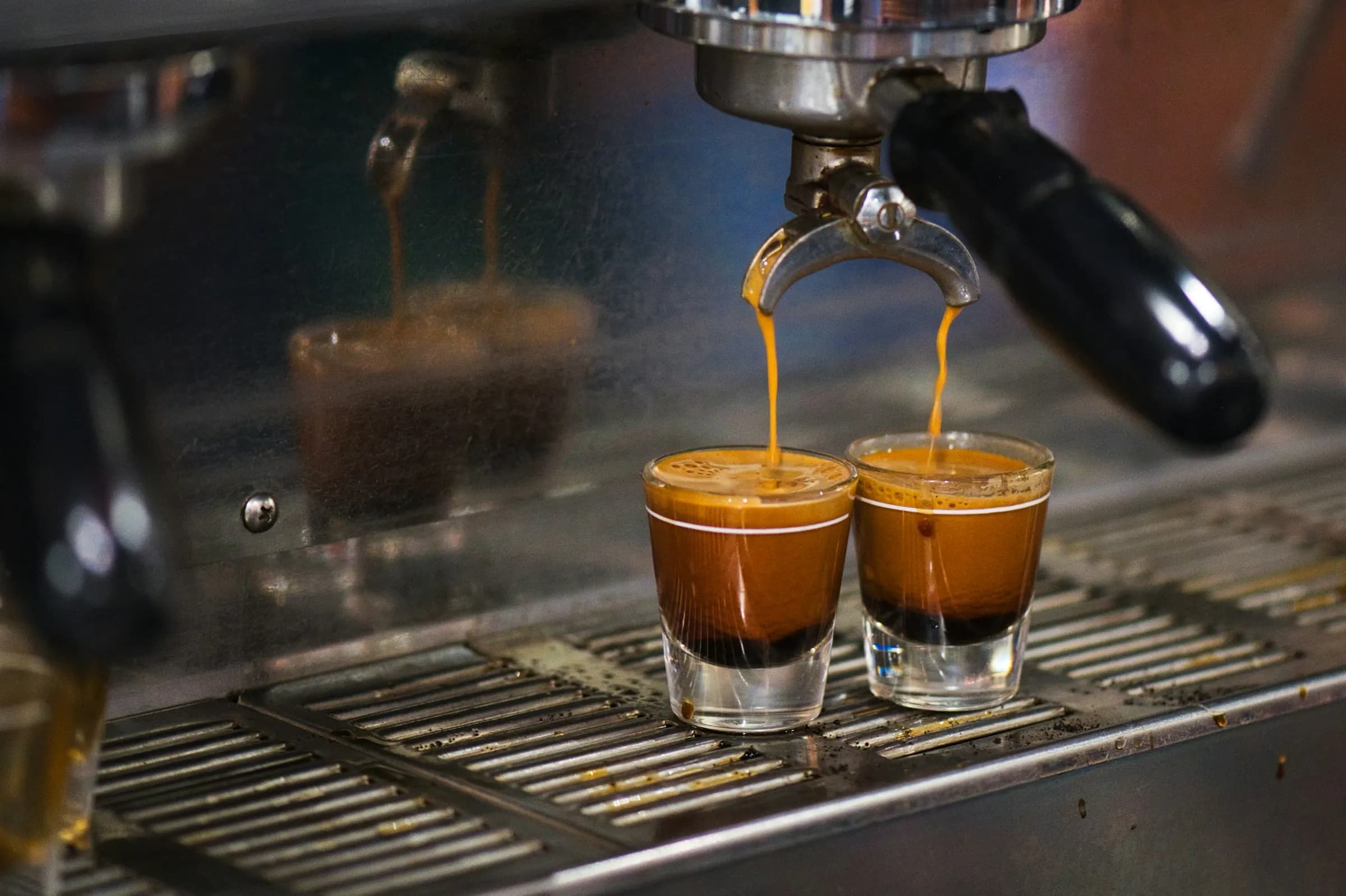 Two espresso shots pouring from a portafilter into small glasses on a steel machine